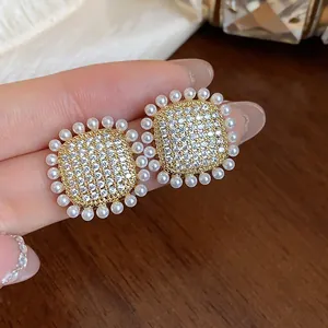 Macro view of square zircon stud earrings with small white pearls on a female hand.