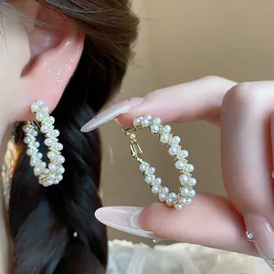 Close-up of elegant gold hoop earrings with white pearls and zircons on model