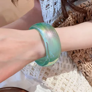 Primer plano de un brazalete ancho transparente verde iridiscente puesto en la muñeca