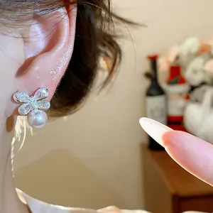 Close-up view of a silver butterfly zircon earring with a dangling pearl on ear.