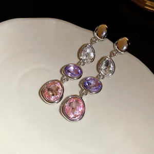 Dettaglio di orecchini pendenti con cristalli a goccia e ovali su un piatto in ceramica