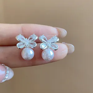 Close-up of butterfly stud earrings with sparkling zircons and white pearl drops