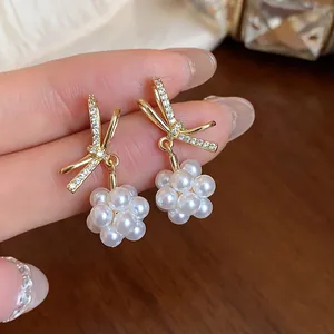 Elegant gold bow earrings with sparkling zircons and delicate white pearl clusters close-up