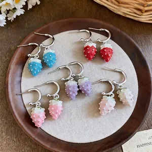 Sweet colorful enamel strawberry dangle earrings presented on a rustic wooden tray