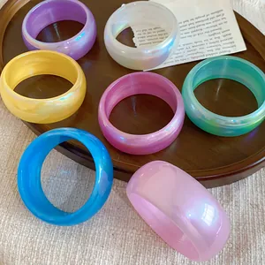 Primer plano de pulseras de resina iridiscentes coloridas en una bandeja de madera con luz.