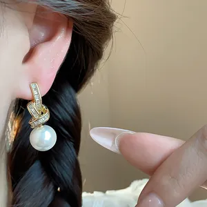 Close-up of elegant gold zircon pearl drop earring worn on a female ear
