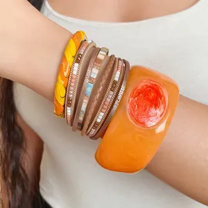 Primo piano di un bracciale in resina arancione retrò e braccialetti a strati sul braccio di donna