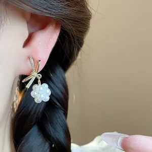 Close-up of elegant gold bow earrings with a delicate pearl flower cluster on an ear.
