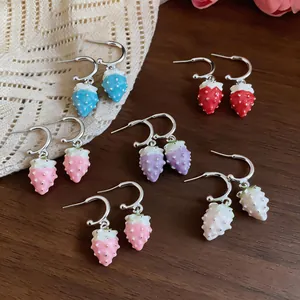 Detail view of colorful enameled strawberry drop earrings on a rustic wood background