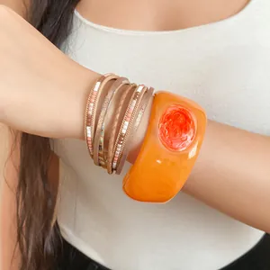 Dettaglio del bracciale rigido in resina arancione e braccialetti avvolgenti