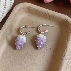A detailed view of sweet purple oil-dripped strawberry pendant earrings on a beige tray.