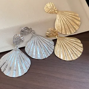 Detailed view of large gold and silver seashell drop earrings with textured finish