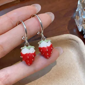 Detail view of sweet red and white enamel strawberry drop earrings being held in hand