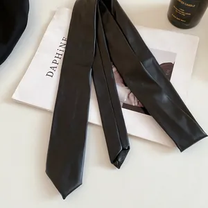 Close-up of a minimalist black faux leather necktie necklace on a lifestyle prop background
