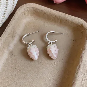 Close-up of sweet strawberry dangle earrings with pink enamel on a textured tray