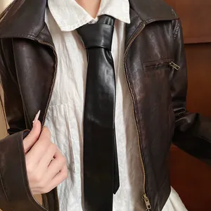 Close-up of vintage black leather tie necklace styled with a classic brown leather jacket detail