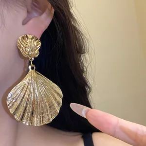 Detailed close-up showing texture of vintage gold metallic pleated shell drop earrings on model