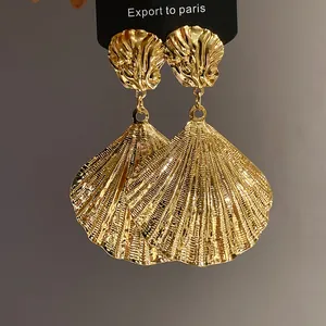 Close-up of vintage gold pleated shell dangle earrings on a black display card.