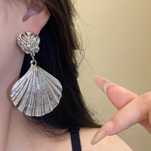 Close-up view of vintage silver metallic pleated shell dangle earrings worn by a model