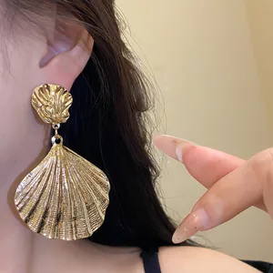 Close-up of vintage golden metal pleated shell earrings on model's ear showing fine texture