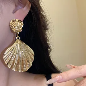 Close-up of a large gold shell drop earring worn by a model showcasing metallic texture