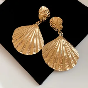 Detailed macro view of vintage gold pleated shell pendant earrings on a black display pad.