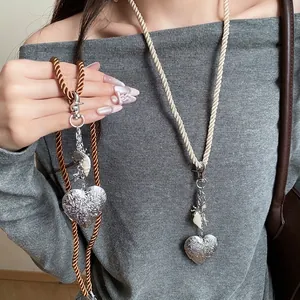 Long rope cord necklace with silver heart locket and ocean shell charms details.