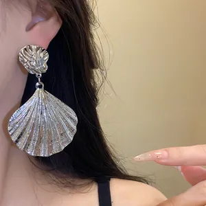 Close-up of large silver metallic shell drop earrings with pleated vintage texture