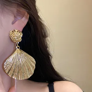 Detailed macro view of vintage gold metallic pleated seashell pendant earrings on model