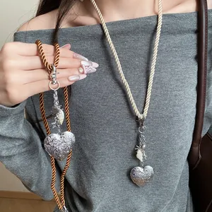Close-up of vintage engraved silver heart pendant with braided rope cord and sea shells.