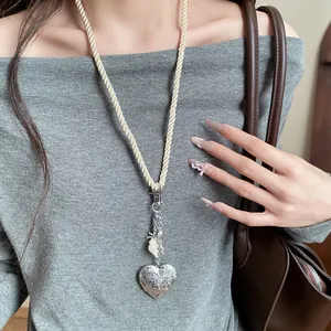 Close-up of long cord necklace with silver heart pendant and shell charms on model
