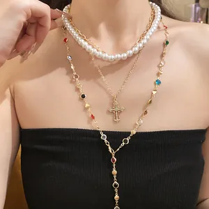 Detailansicht einer goldenen Mehrlagenkette mit Harzperlen und Kristallkreuz-Anhänger