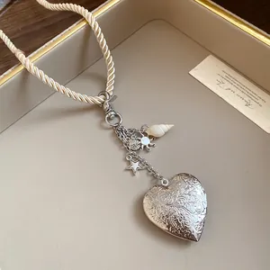 Detail shot of a vintage silver heart locket necklace with rope cord and shell charms