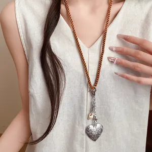 Detail of a long brown cord necklace with a silver heart pendant and shell charm on model