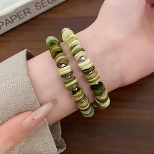 Detailed close-up of shell disc beaded bracelets in green and cream on wrist