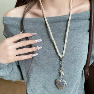 Detail view of a long rope necklace with a vintage silver engraved heart pendant