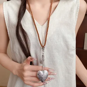 Close-up view of a vintage engraved silver heart pendant on a stylish brown rope cord