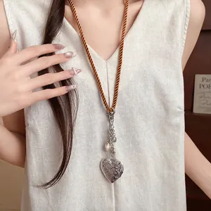 Detail of a long rope necklace with an engraved silver heart locket and shell charms.