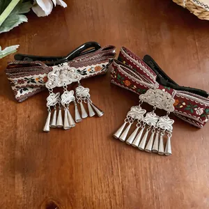 Detail of vintage Bohemian woven hair clips with silver metal tassels on wood background.