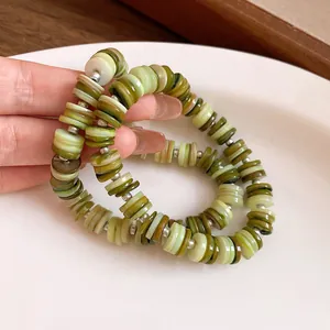 Detail shot of multi-layer shell beaded necklace with green disc beads and silver accents
