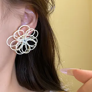 Detail view of a large white spray-painted hollow flower wire stud earring on ear