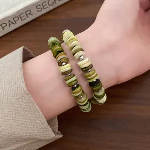 Close-up of olive green and cream shell beaded multi-layer bracelets worn on a wrist