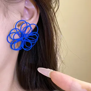 Macro view of unique blue hollowed-out wire flower stud earrings worn by a model
