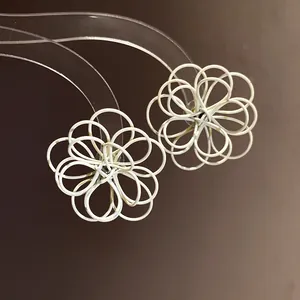 Close-up of elegant white spray-painted wire-wrapped hollow flower stud earrings.