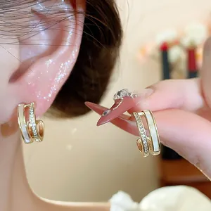 Detailed close-up of double-layer C-shaped gold earrings with mother-of-pearl and zircon