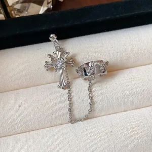 Detail view of a silver cross earring and butterfly ear cuff connected by a metal chain.