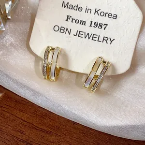 Detail of 14k gold-plated C-shape earrings with shell inlay and zircons on display card