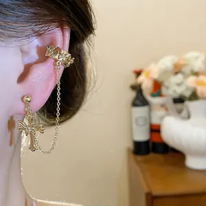 Close-up of gold-plated cross earring with chain and ear cuff jewelry
