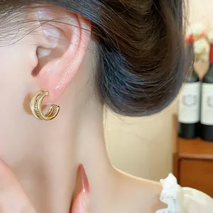 Close-up detail of double-layered gold C-shaped earrings with micro-zircons.