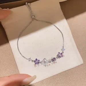Detail of adjustable silver bracelet with purple and white zircon flower charms.